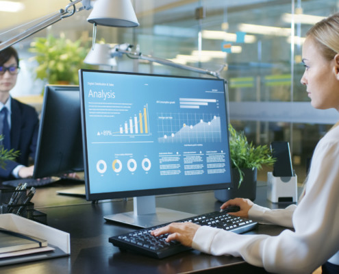 Financier Works on a Personal Computer Showing Statistics, Graphs and Charts. In the Background His Coworker and Creative Office.